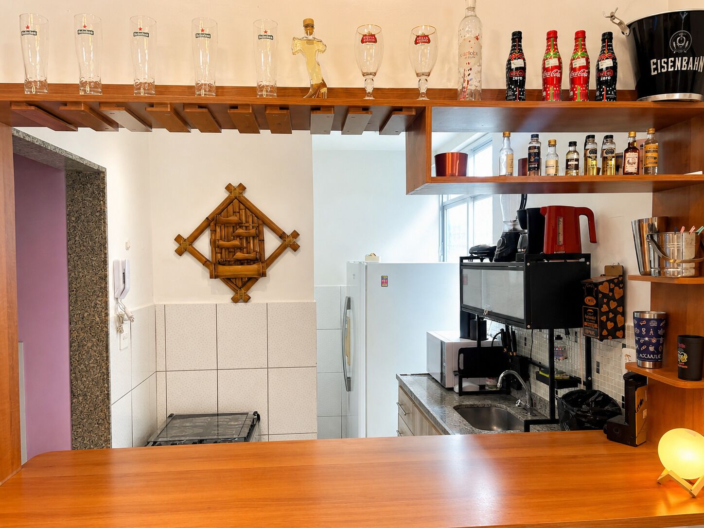 Une cuisine avec un plan de travail en bois, une machine à café et des étagères remplies de bouteilles et de verres.