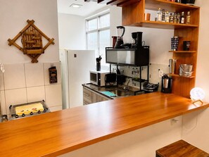 Una cucina con piano di lavoro in legno, microonde, macchina da caffè ed uno scaffale con bottiglie.