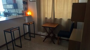 Una pequeña kitchenette con microondas, cafetera y lavamanos. Hay dos taburetes y una mesa con una silla.