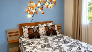 Un dormitorio con cama, mesita de noche, lámpara de pared y ventana con cortinas.