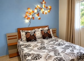 A bedroom with a bed, a nightstand, a wall-mounted light fixture, and a window with curtains.