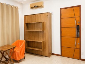 A room with a wooden wardrobe, a small table with a chair, and a door with a handle.