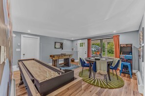 A room with a foosball table, a dining table with chairs, and a window with curtains. - Sauna •  Hot Tub • Game Room • Theater •  Firepit (Bethel)