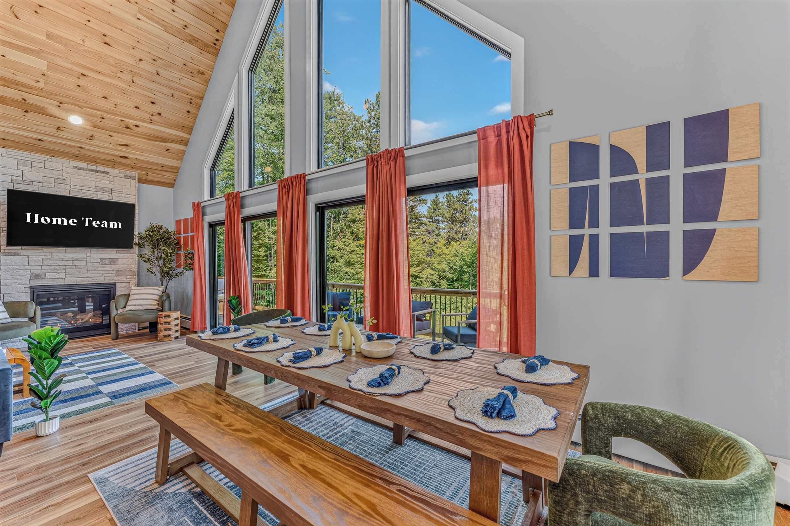 A modern living room with a fireplace, a dining table set for six, and a large window with curtains.