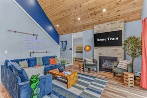 A modern living room with a blue sofa, a wooden coffee table, and a fireplace. - Sauna •  Hot Tub • Game Room • Theater •  Firepit (Bethel)