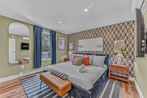 A bedroom with a bed, a bench, a nightstand, a mirror, and a wall with a geometric pattern. - Sauna •  Hot Tub • Game Room • Theater •  Firepit (Bethel)