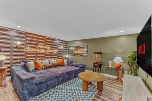A living room with a sofa, a coffee table, a TV, and a wall with a neon sign. - Sauna •  Hot Tub • Game Room • Theater •  Firepit (Bethel)