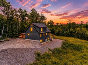 A two-story cabin with a porch and a gravel driveway. - Sauna •  Hot Tub • Game Room • Theater •  Firepit (Bethel)