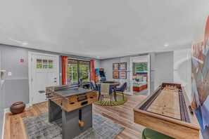 A room with a foosball table, a ping pong table, and a billiards table. There are windows with curtains, a door, and a wall with framed pictures. - Sauna •  Hot Tub • Game Room • Theater •  Firepit (Bethel)