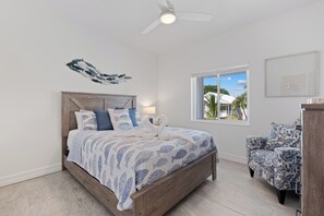 A bedroom with a bed, a ceiling fan, a window with a view, and a chair. - 🌞🌴Pearl Street Retreat | Heated Pool + Steps to Beach (Fort Myers Beach)