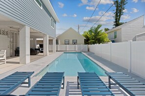 A swimming pool with lounge chairs, a covered patio area, and a white fence. - 🌞🌴Pearl Street Retreat | Heated Pool + Steps to Beach (Fort Myers Beach)
