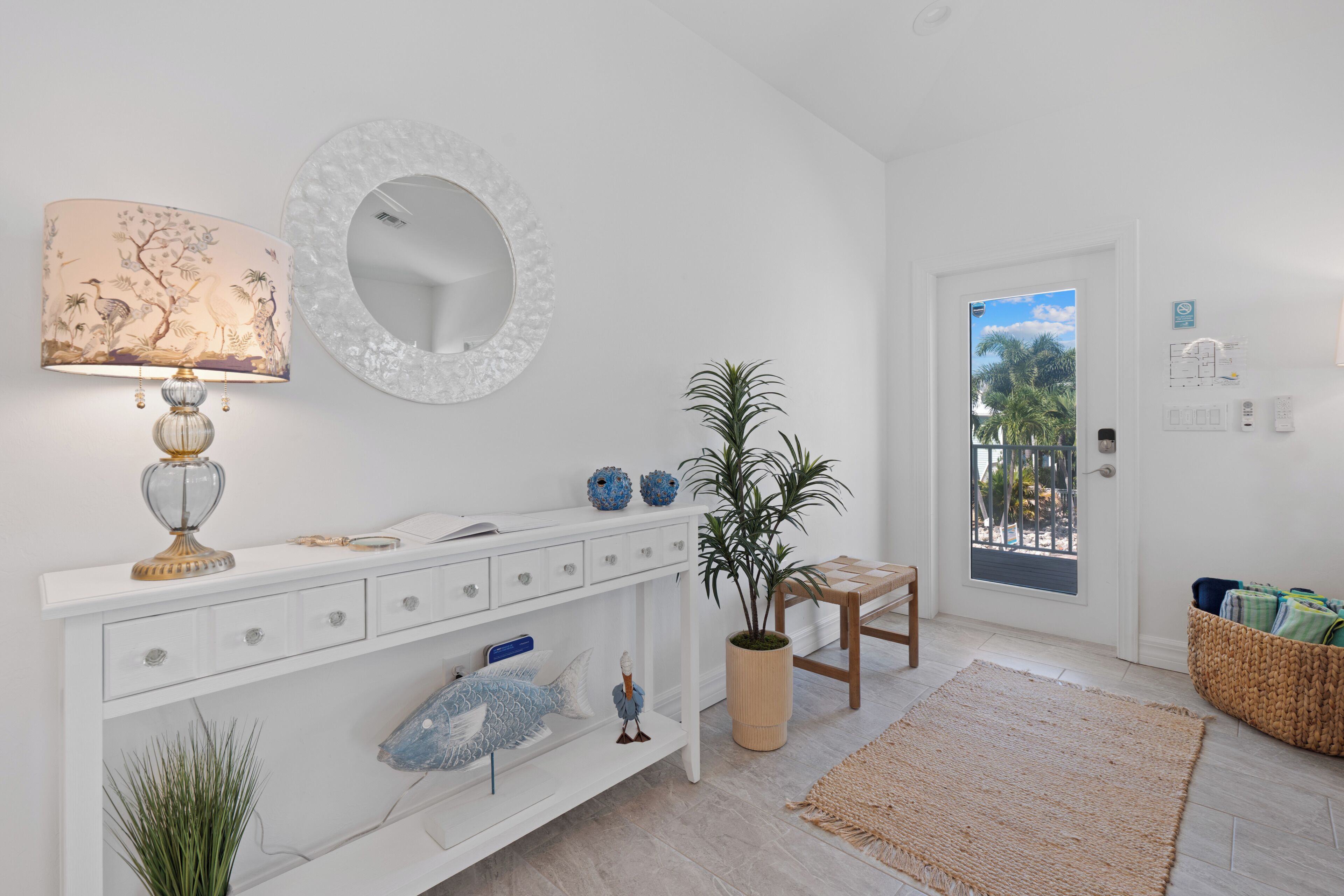 Ein modernes Interieur mit einer weißen Konsole, einem Spiegel, einer Lampe, Dekorationselementen, einer Topfpflanze, einem Holzstuhl und Blick durch eine Tür.