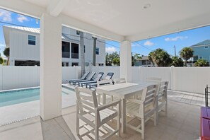 A covered outdoor area with a pool, white furniture, and a view of a residential building. - 🌞🌴Pearl Street Retreat | Heated Pool + Steps to Beach (Fort Myers Beach)