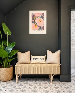 Ein Zimmer mit dunklen Wänden, einem gewebten Sofa, einer Topfpflanze und einem gerahmten Kunstwerk.