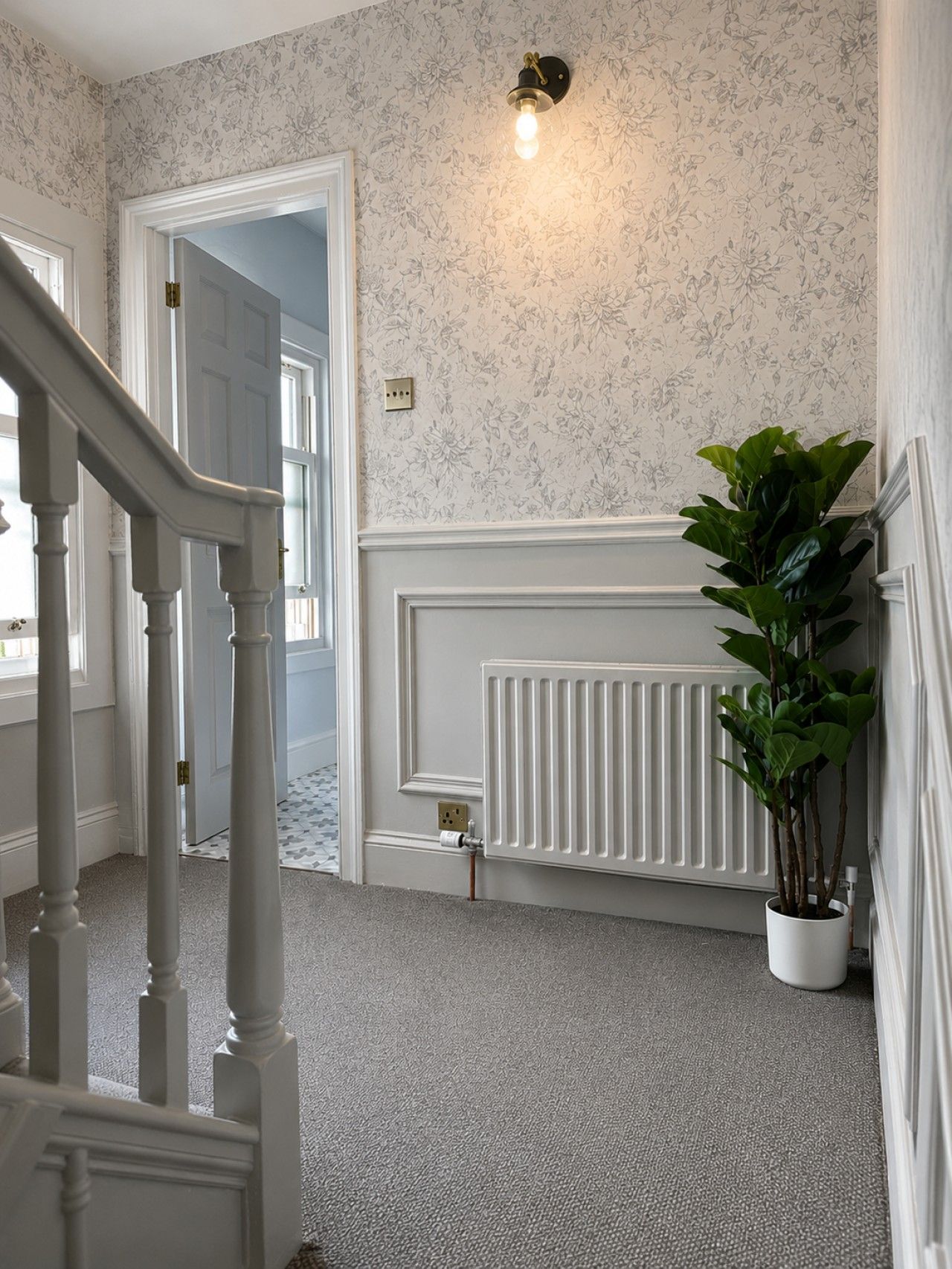 A hallway with a white radiator, a potted plant, and a staircase.