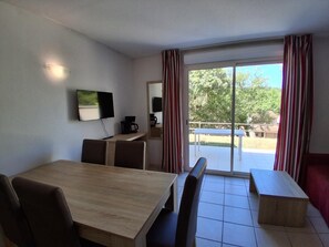 En matplats med ett bord och stolar, en tv som är monterad på väggen och utsikt över utomhusmiljön genom en skjutdörr i glas.