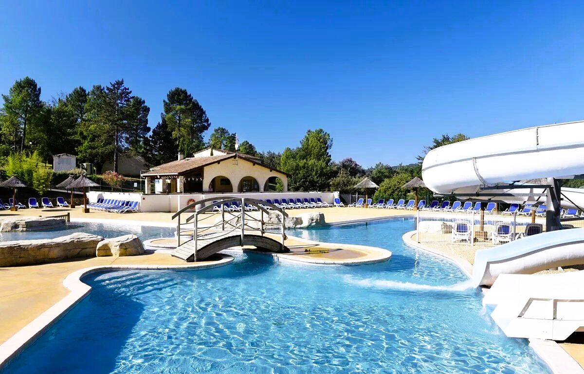 A swimming pool with a bridge, lounge chairs, and a water slide.