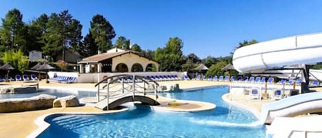 A swimming pool with a bridge, lounge chairs, and a water slide.