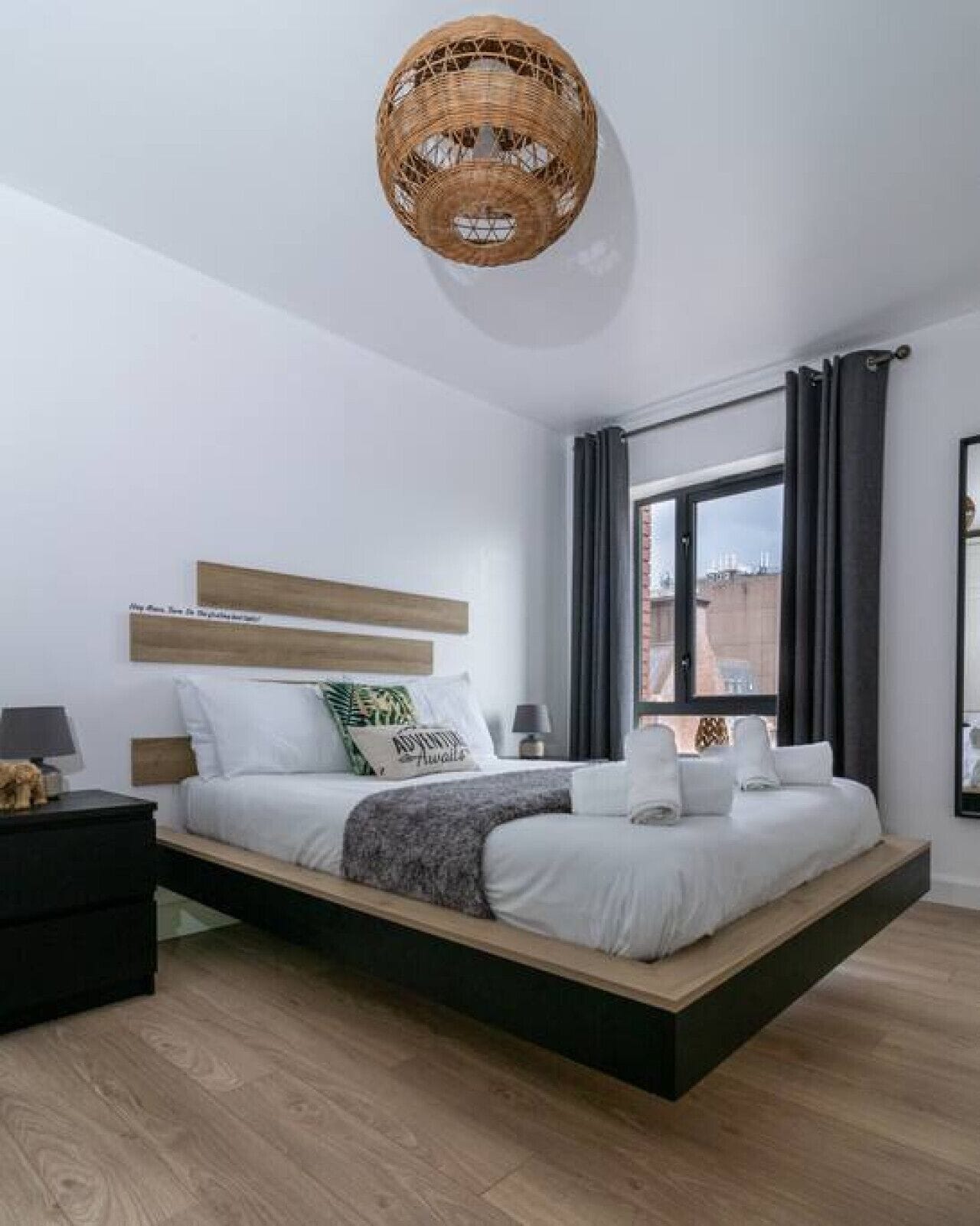 A modern bedroom with a floating bed, a bedside table, a lamp, and a view of the city through a window.