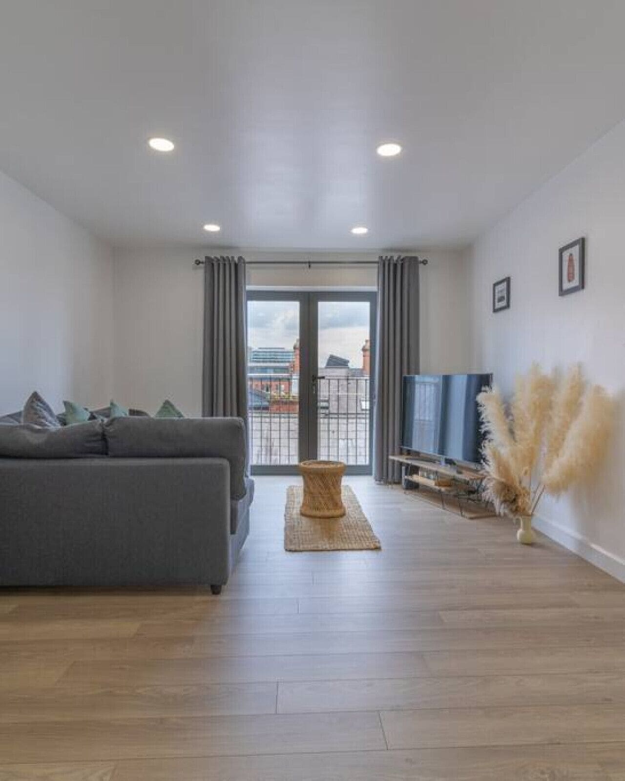 Un salon moderne avec un canapé gris, une table basse en bois et une vue à travers une porte vitrée.