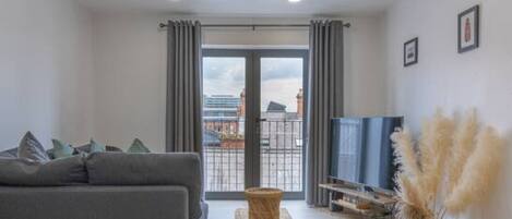 A modern living room with a grey sofa, a wooden coffee table, and a view through a glass door.