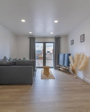 Ein modernes Wohnzimmer mit grauem Sofa, einem Holztisch und Blick durch eine Glastür.
