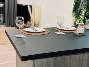 Ein Esstisch mit zwei Gedecken, Weingläsern, gewebten Platzsets und einer kleinen Dose Gewürze.