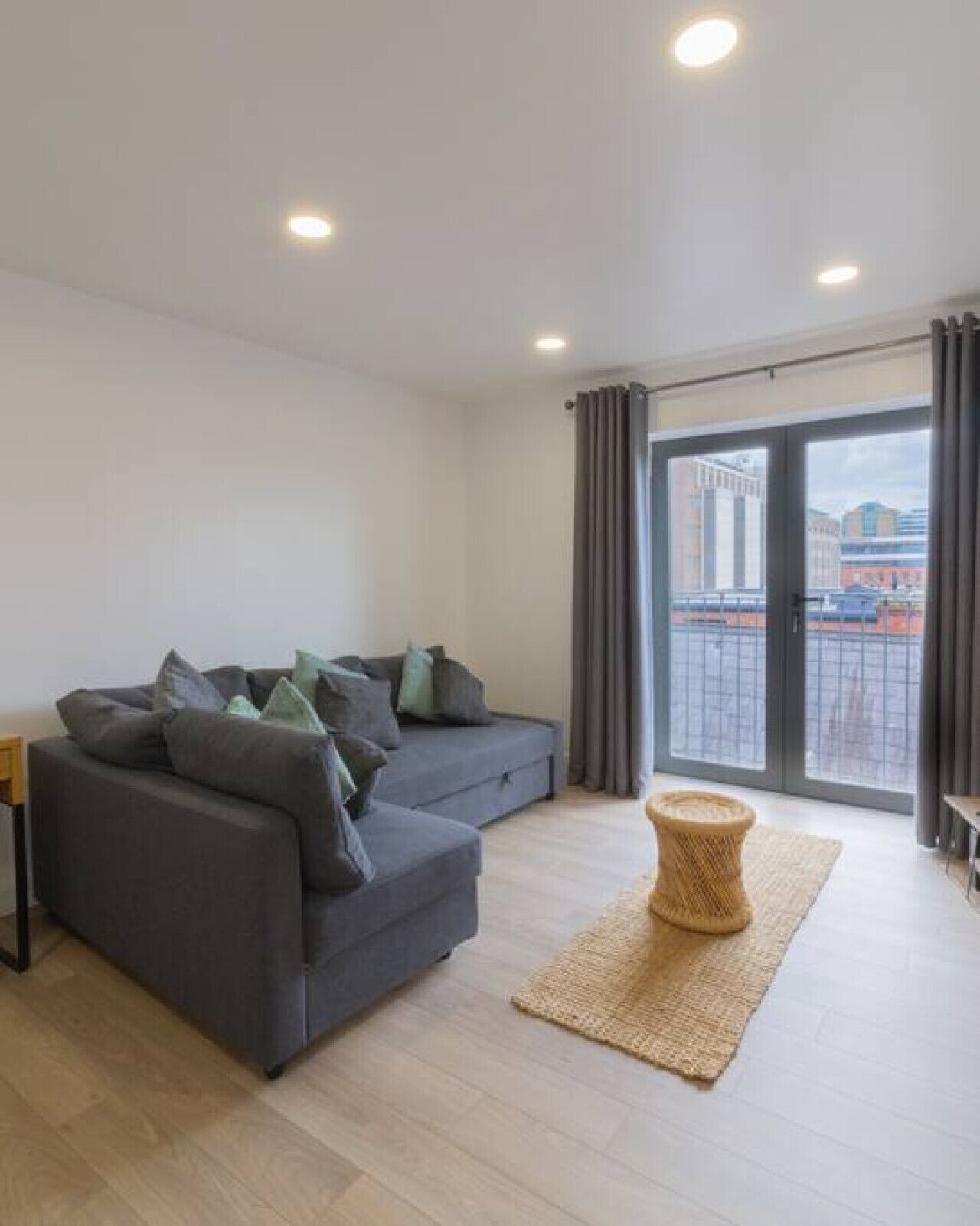 Un salon moderne avec un canapé gris, un tapis en fibres naturelles et une vue à travers une porte vitrée.