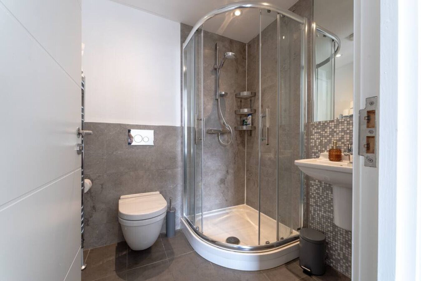 A modern bathroom with a glass-enclosed shower, a toilet, and a sink with a tiled backsplash.