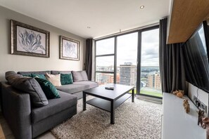 Uma sala de estar moderna com um sofá cinzento, uma mesa de centro e uma grande janela com vista para a cidade.
