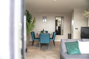 Ein modernes Wohnzimmer mit einem grauen Sofa, Türkis-Farbenen Sesseln und einem Essbereich mit Tisch und Stühlen.