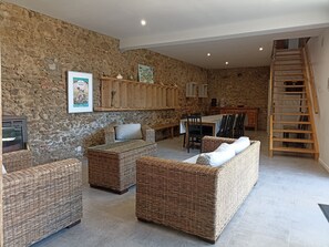 A rustic interior with stone walls, wicker furniture, a dining table, and a wooden staircase.