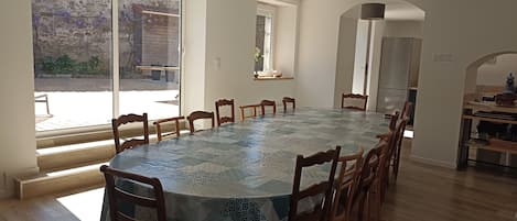 Un espace repas comprenant une longue table, plusieurs chaises et une vue sur l’extérieur grâce à une porte vitrée.