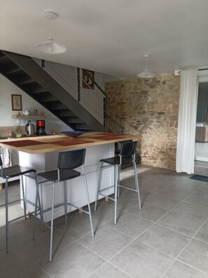 Eine Küche mit einer zentralen Kochinsel, Barhocker, einer Kaffeemaschine und einer Treppe zu einer Mansarde.