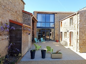 A courtyard with stone buildings, a modern glass door entrance, outdoor seating, and potted plants.