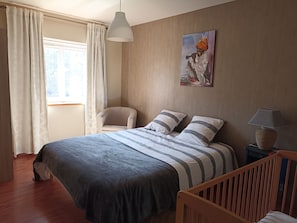 A bedroom with a bed, a chair, a lamp, and a painting on the wall.