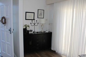Une pièce avec une porte blanche, une commode noire, un chandelier et deux tableaux encadrés accrochés au mur.