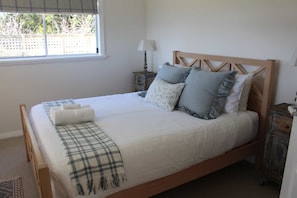 A neatly made bed with a plaid blanket and pillows, a bedside lamp, and a window with a view of trees. - Capbreton Waterfront Retreat (Clarence Point)