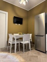 Una cocina moderna con un refrigerador de acero inoxidable, un televisor de pantalla plana montado en la pared y una mesa de comedor con sillas blancas.
