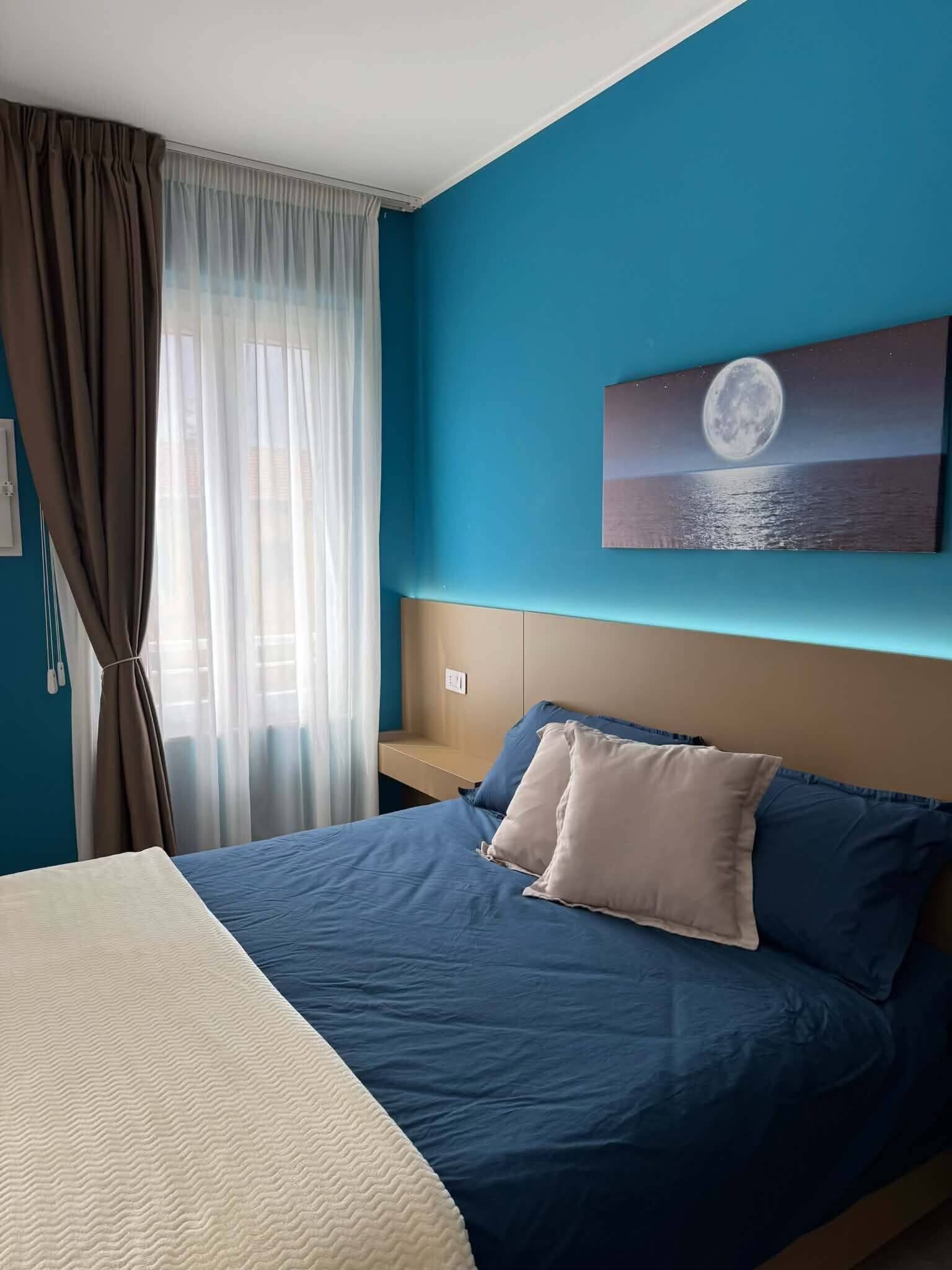 Une chambre d’hôtel avec un lit, un tableau représentant une mer illuminée par la lune et une fenêtre avec des rideaux.