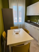 Una cocina compacta con una mesa, sillas, un refrigerador y un ventanal con cortinas.