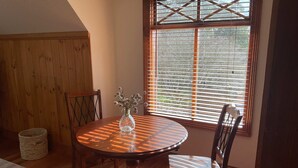 A dining area with a round table, chairs, a vase with flowers, a wooden cabinet, and a window with blinds. - Villa Marche - Taste of Tuscany (Riverside)
