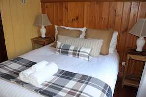 A bed with a plaid blanket, rolled towels, and multiple pillows in a room with wooden paneling and two bedside lamps.