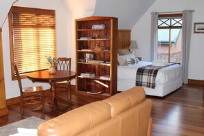 Una habitación acogedora con una cama, una estantería de madera, una mesa de comedor con sillas y una ventana con persianas.