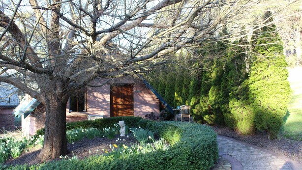 A stone pathway leading to a rustic building with a wooden door, surrounded by lush greenery and a well-maintained garden. - Villa Marche - Taste of Tuscany (Riverside)
