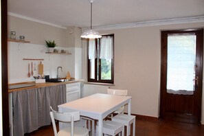 A compact kitchen with a dining table, chairs, a hanging light fixture, and a window with curtains. - BELVEDERE LAKE VIEW VACATION RENTAL (Rocca)