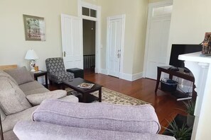 A living room with a sofa, armchair, coffee table, and a television on a stand. - Apartment near Forsyth Park with free parking. 1.3 mile walk to River Street (Savannah)