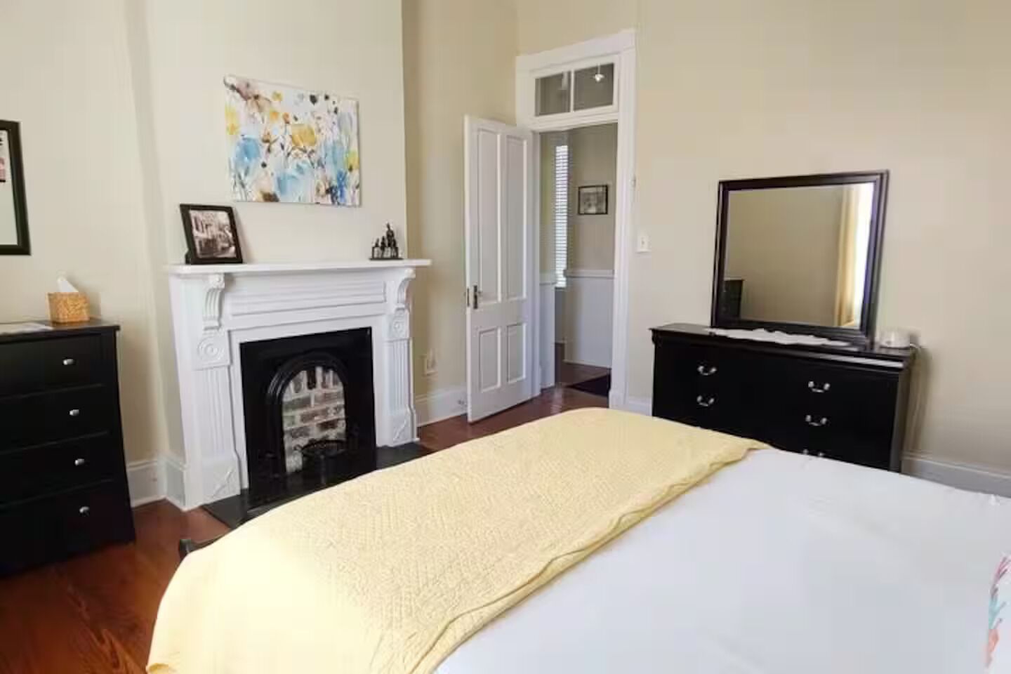 Une chambre à coucher comprenant un lit, une cheminée, une commode, un miroir et une porte donnant sur une autre pièce.
