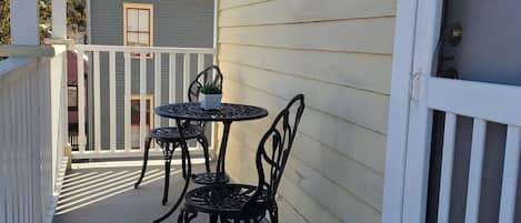 Un pequeño patio exterior con una mesa y sillas, un felpudo y una casa con techo rojo al fondo.