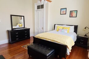 Ein Schlafzimmer mit einem Bett, einem Schminktisch, einer Bank, einer Tür und zwei Wandbildern.